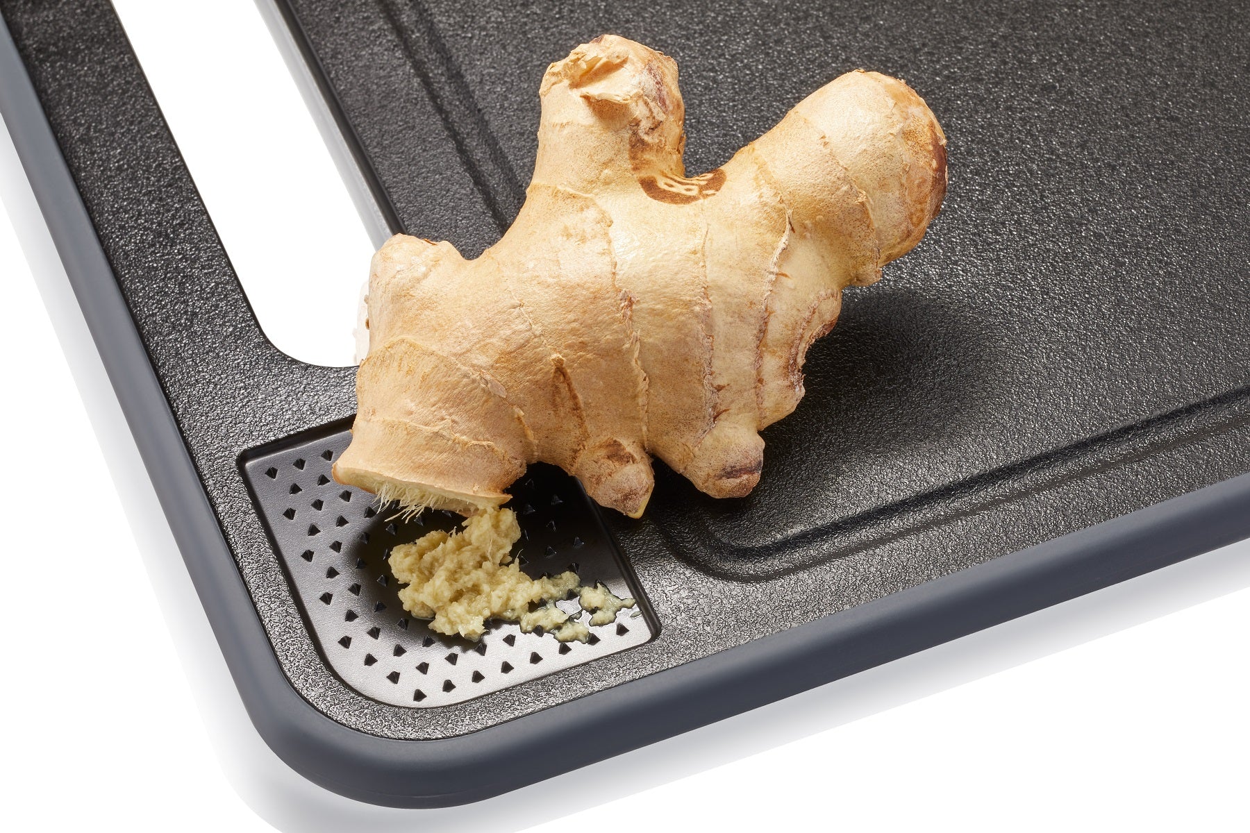 Detailaufnahme des Michelino 4in1 Schneidebretts mit integrierter Reibe, auf der frischer Ingwer zerkleinert wird.