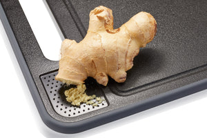 Detailaufnahme des Michelino 4in1 Schneidebretts mit integrierter Reibe, auf der frischer Ingwer zerkleinert wird.